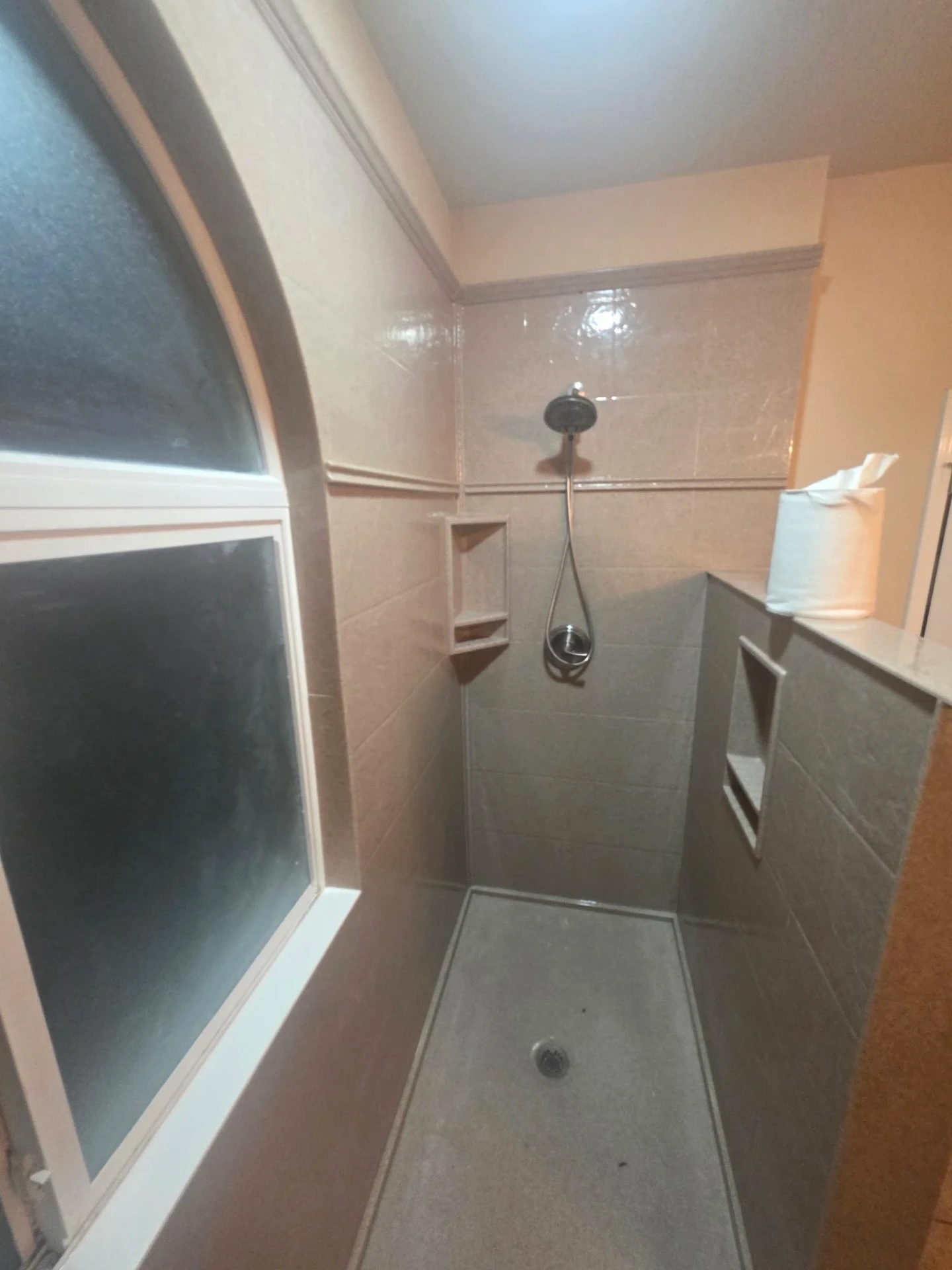 Curbless walk-in shower with two-tone tile, recessed soap niche and arched glass-block window — full bathroom conversion by Hector