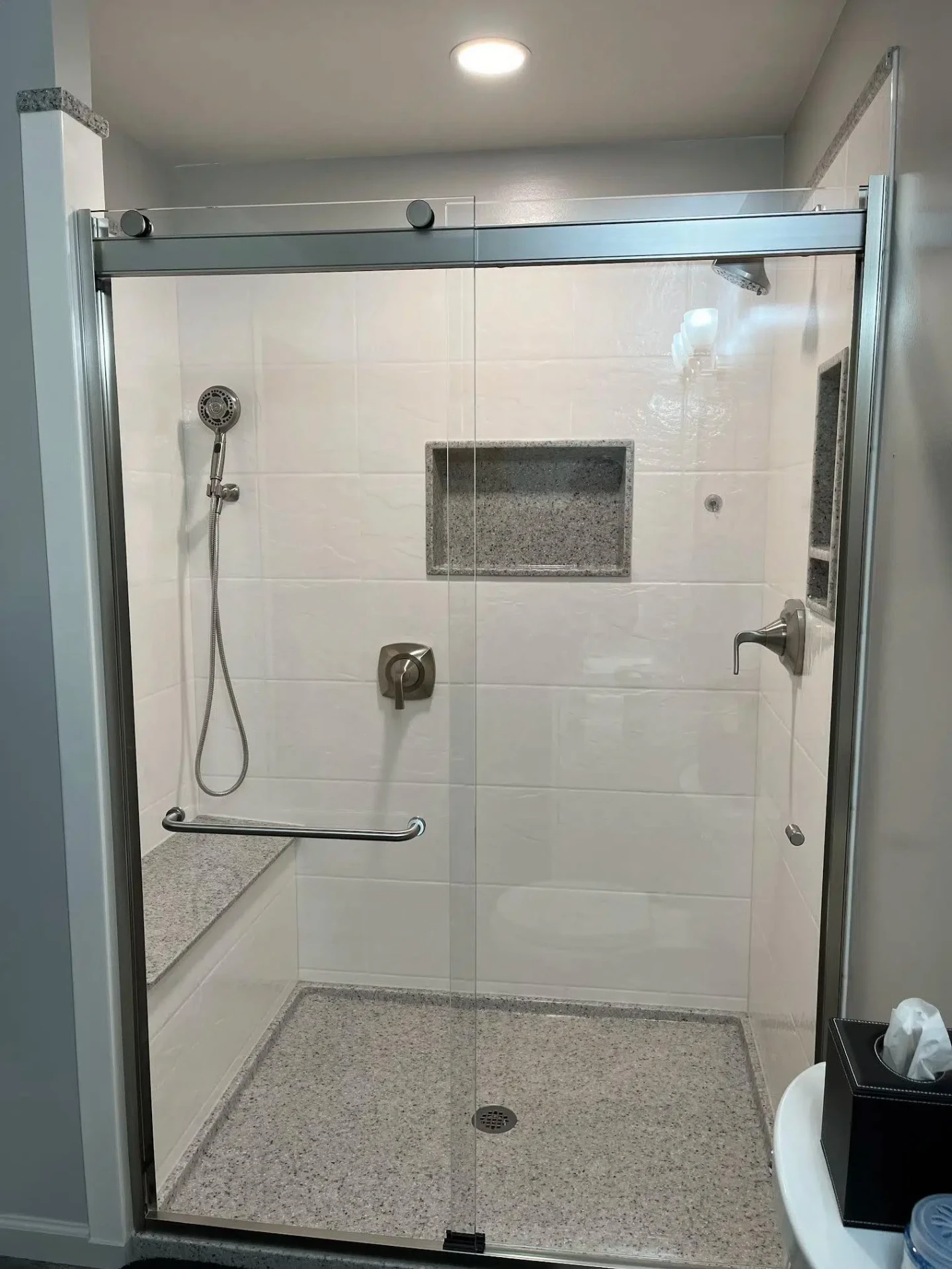 White subway-tile shower with frameless sliding glass door, granite bench and matching recessed niche installed in a San Antonio area home