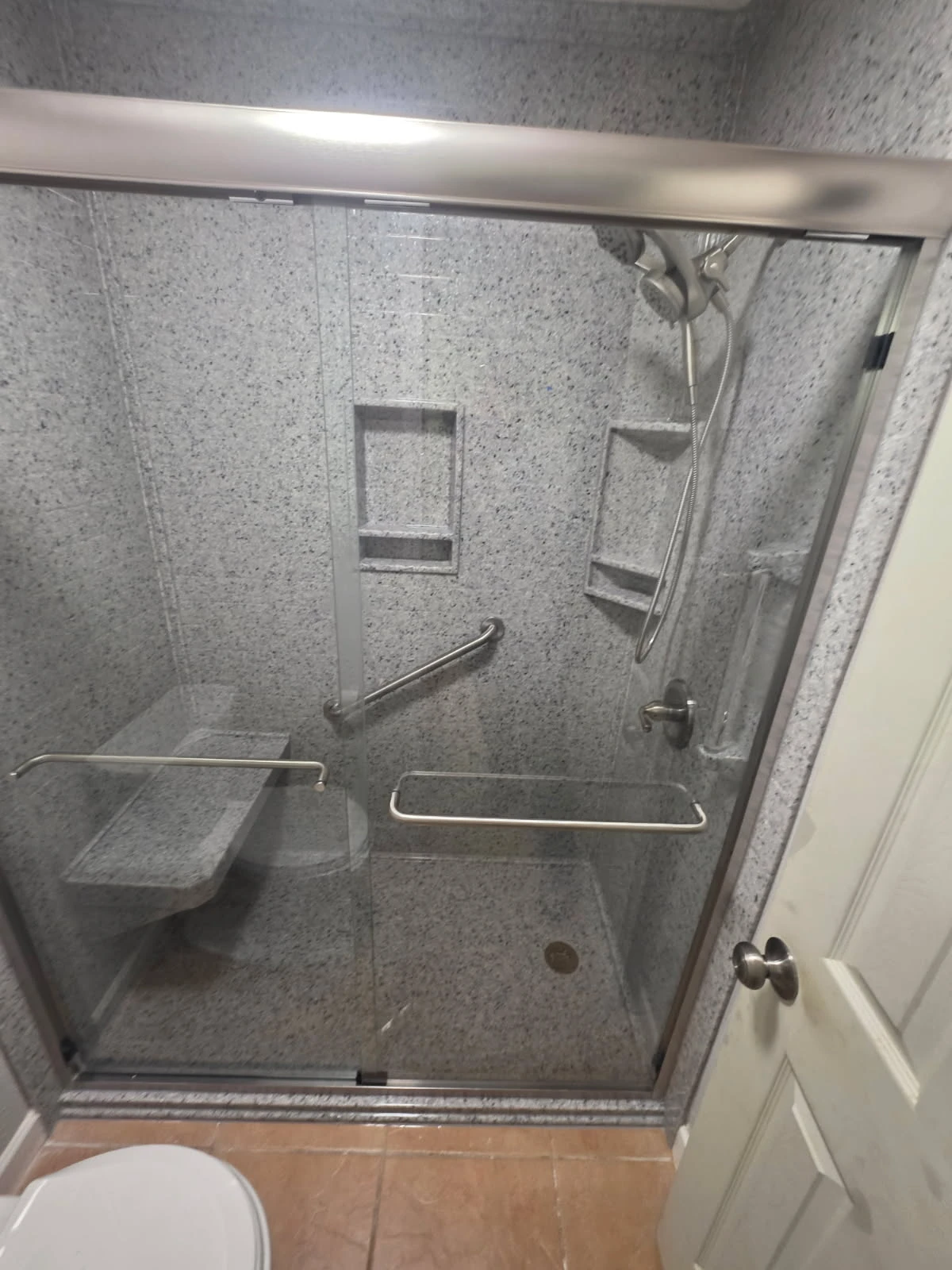 Gray granite-pattern walk-in shower with bypass glass doors, fold-down bench and dual recessed niches