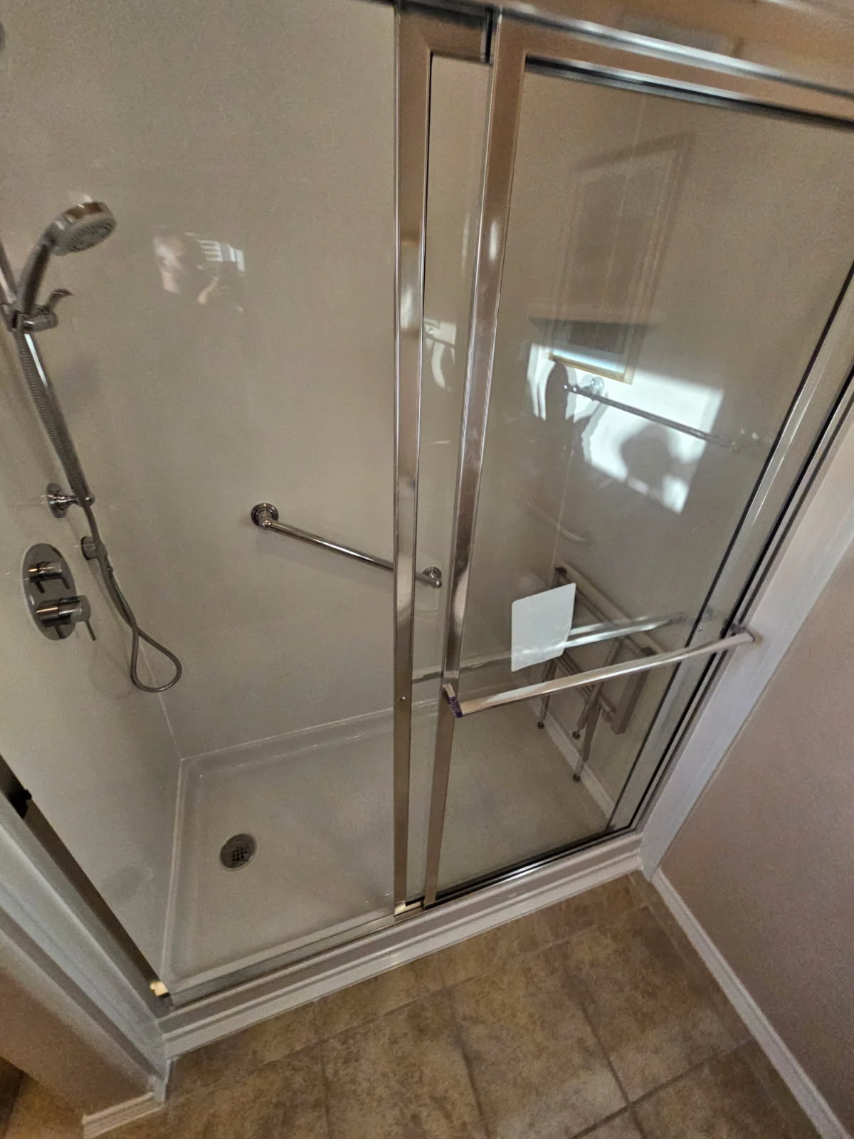 Clean white solid-surface shower with chrome bypass glass doors, handheld sprayer and ADA grab bar installed in a San Antonio bathroom