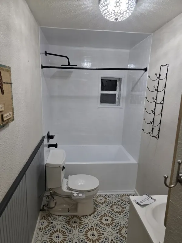 White subway-tile tub-and-shower combo with matte black rain shower, tub filler and shower rod over patterned Moroccan-tile floor — full bathroom remodel by Out This World Services